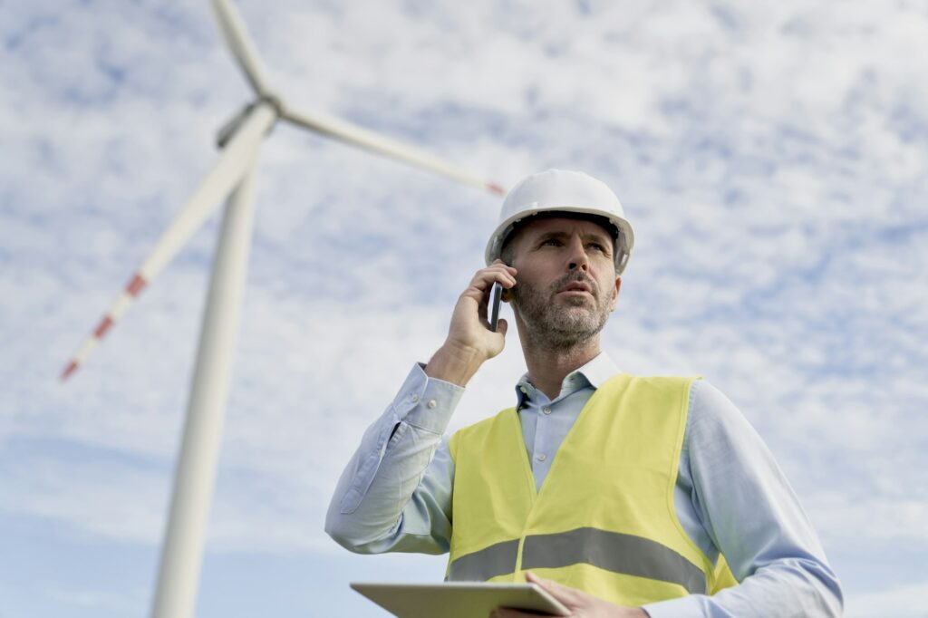 Caucasian male engineer standing on wind turbine field with digital tablet and talking on the phone