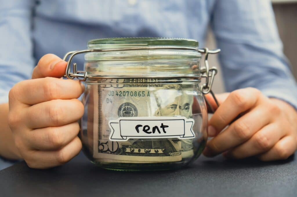 Female hands holding Glass jar full of American currency dollars cash banknote with text RENT