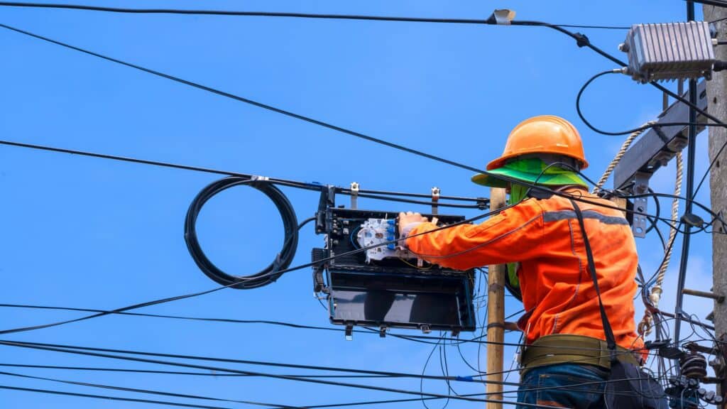 technician installing fiber optic and splitter box on electric power pole