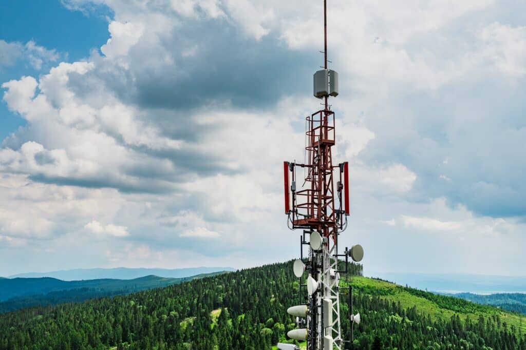 Telecommunication transmitter tower with antennas of cellular communication in mountains against sky