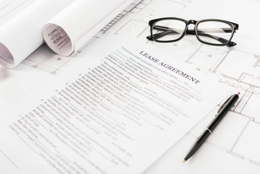 document with lease agreement lettering near glasses, blueprints and pen on desk