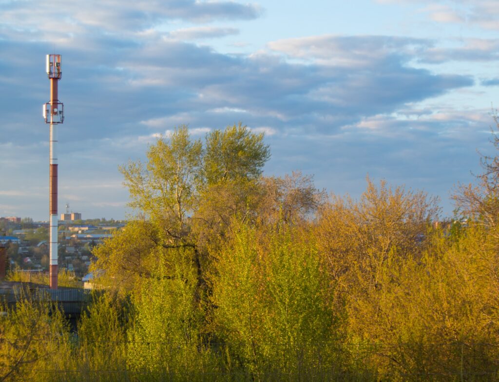 Cell tower of mobile communication on the background of trees and cloudy sky