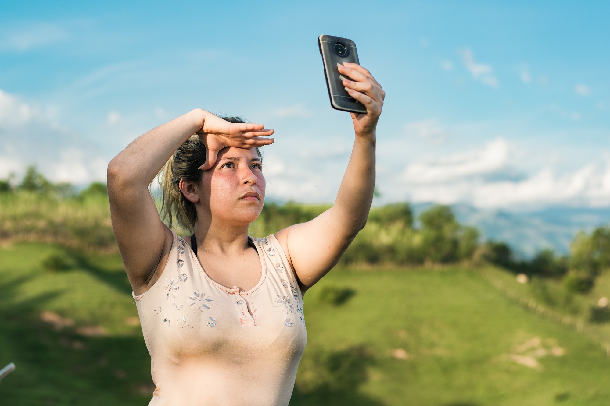 young latina woman on top of a colombian mountain looking for a signal for her mobile phone