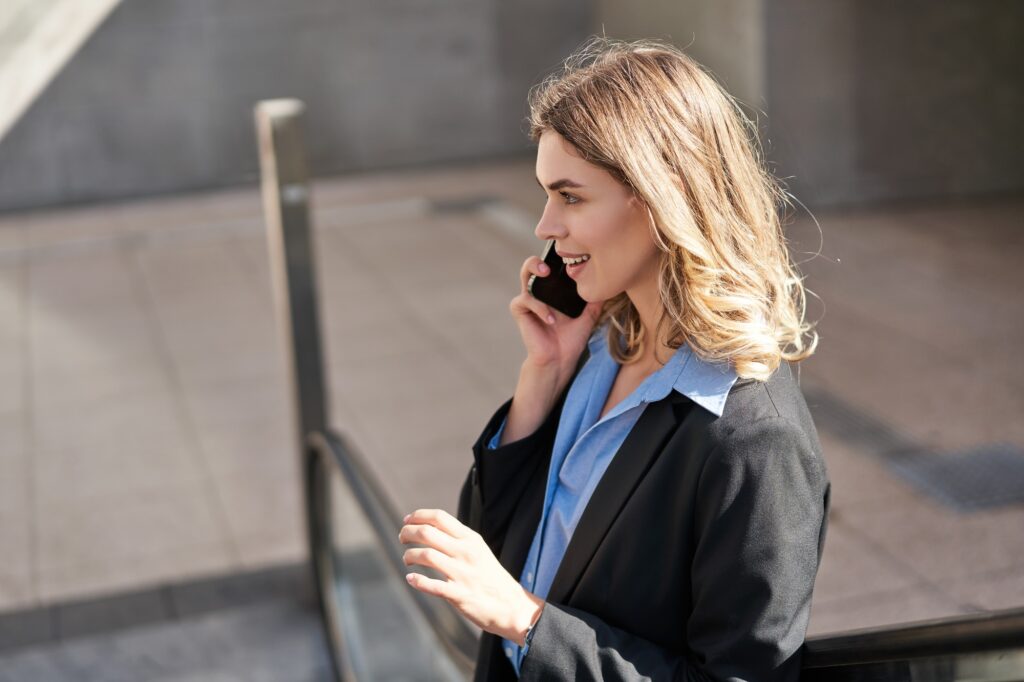 Corporate woman talking on mobile phone, making a call while in city, standing outdoors on