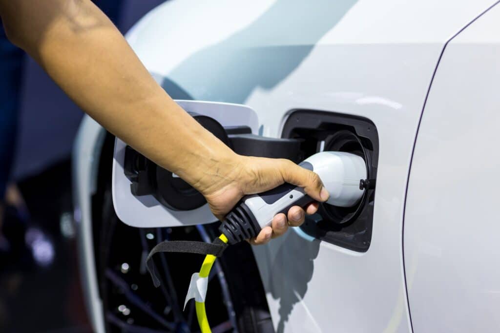 Hand Holding Electric Car Charger. Electric Vehicle Ev Charging Station And Charger.